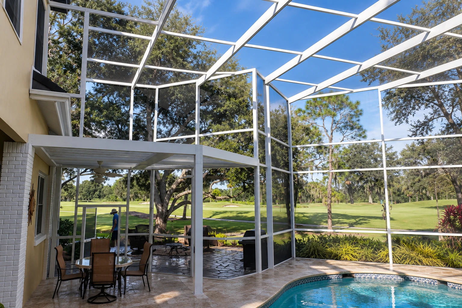 A white-framed screened patio enclosure with a peaked roof opens onto a lawn and pool, with a dining area beneath the cover.