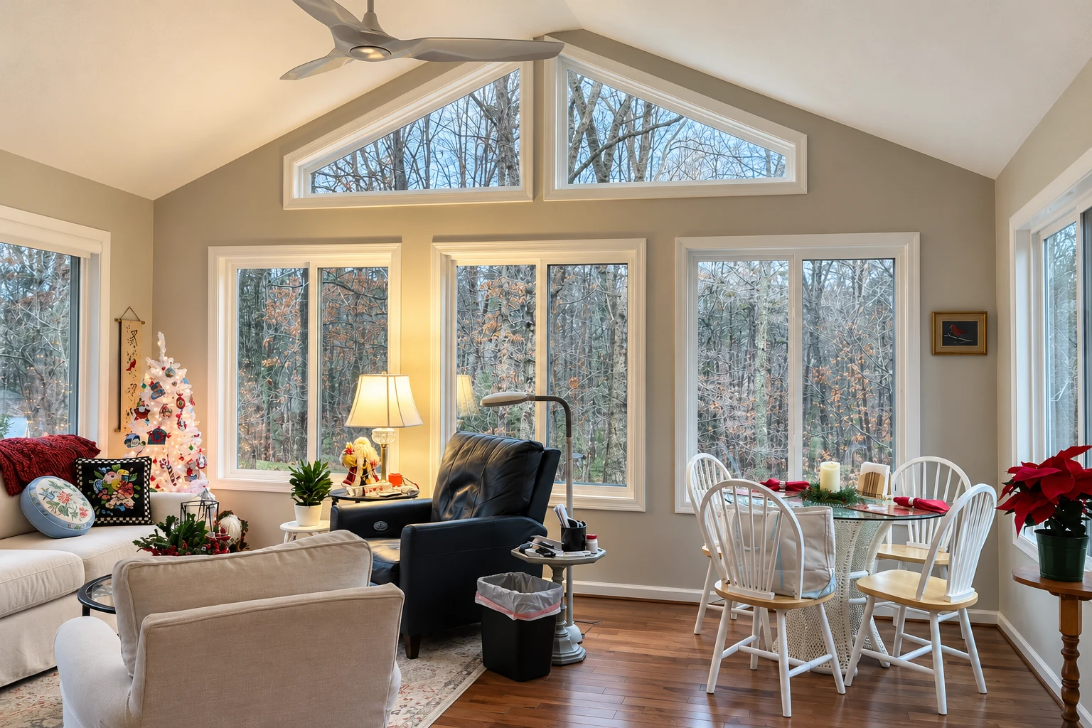 Bright sunroom with high triangular windows, a ceiling fan, and living and dining areas decorated for Christmas.